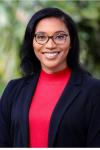 Black woman wearing glasses, a red shirt and a black blazer in front of a green background