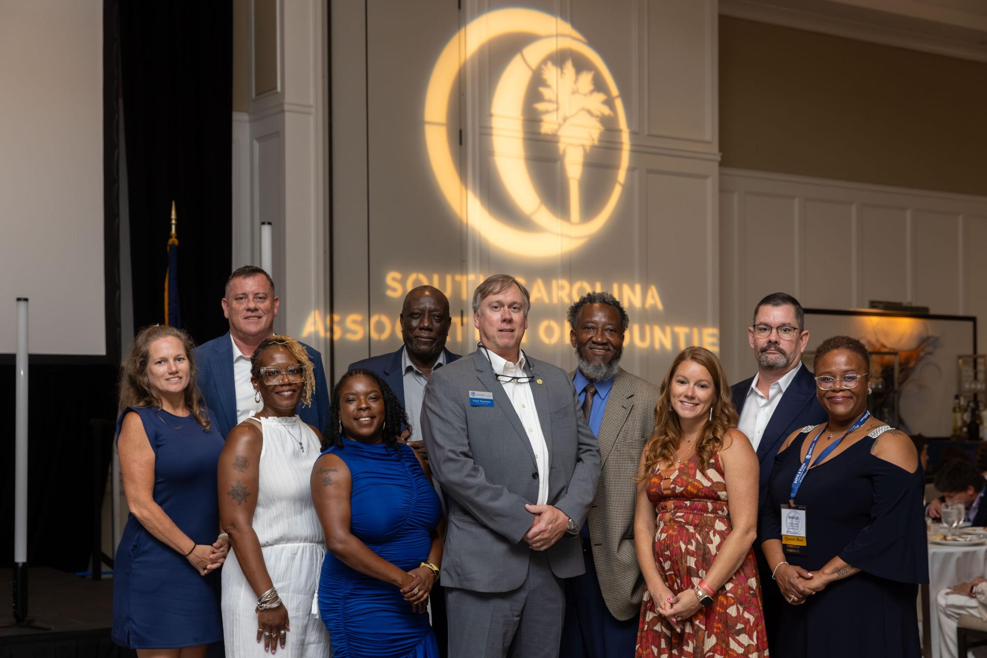 A group of representatives from Calhoun County with Cecil Thornton in the center stand in front of the SCAC logo, projected behind them.